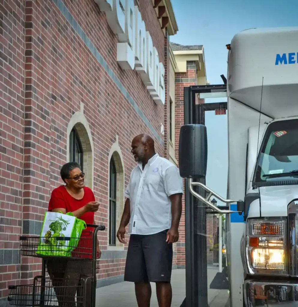 Photo of MMSNYS driver and woman client with MMSNYS transport van man and woman standing in front of a truck.